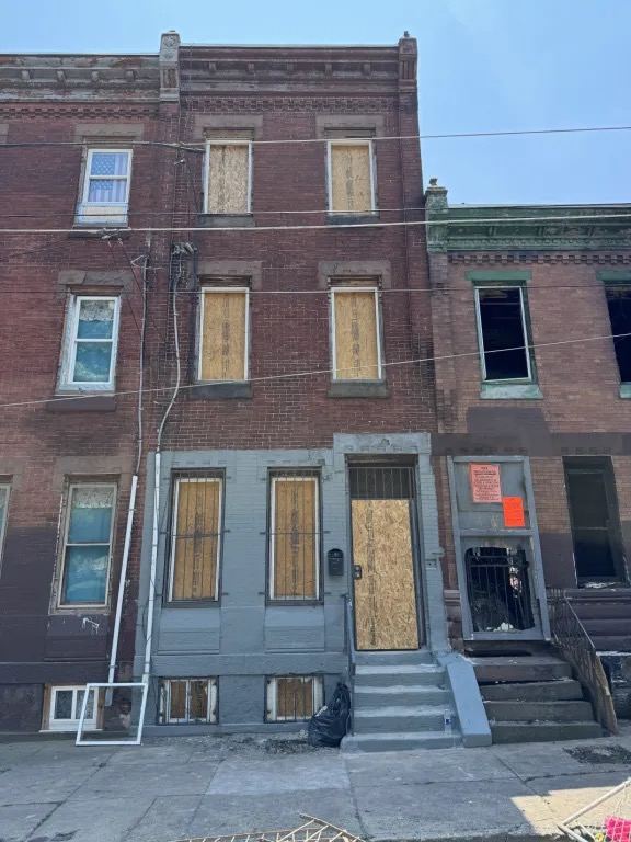 The same brick rowhouse with plywood covering the windows on every floor and the front door.