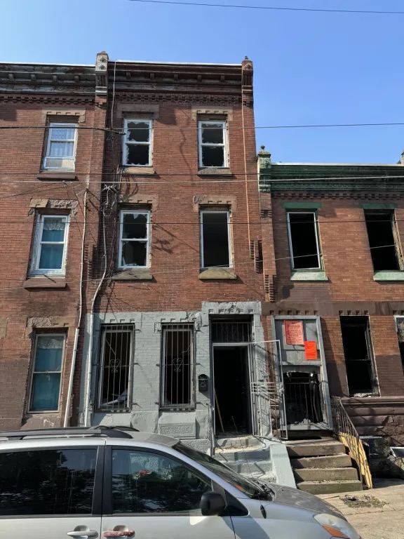 Three story brick rowhouse with broken windows on every floor and an open front doorway.